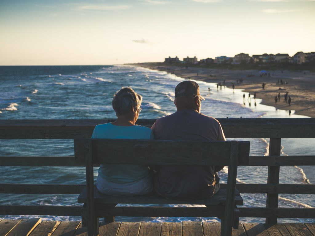 deux personnes âgées assis sur un banc au bord de la mer et regardant la plage